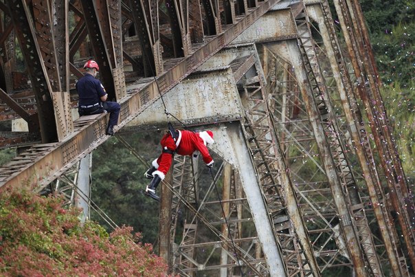 Пожарный Эктор Чакон в костюме Санта-Клауса спускается c моста, чтобы подарить подарки живущим внизу детям, Гватемала.
