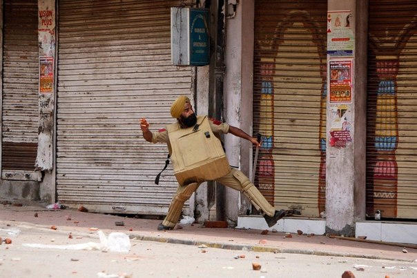 Полицейский, бросающий камни в протестующих, Джамму, Индия. 