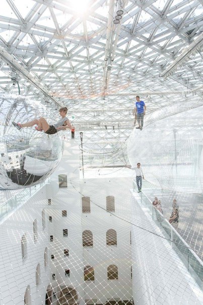В художественном музее в Дюссельдорфе открылась необычная инсталляция, по которой можно и нужно полазить. Под куполом здания на высоте более 20 метров натянули 3 уровня сетки, разделенных между собой огромными прозрачными и зеркальными воздушными шарами. Подобно паукам, люди могут перемещаться по воздушной конструкции, не видя почвы под ногами, балансируя на раскачивающейся сетке.