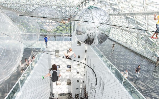 В художественном музее в Дюссельдорфе открылась необычная инсталляция, по которой можно и нужно полазить. Под куполом здания на высоте более 20 метров натянули 3 уровня сетки, разделенных между собой огромными прозрачными и зеркальными воздушными шарами. Подобно паукам, люди могут перемещаться по воздушной конструкции, не видя почвы под ногами, балансируя на раскачивающейся сетке.