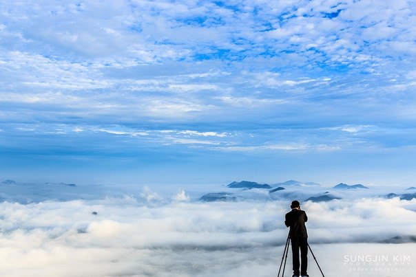 Мужчина фотографирует облака над городом с горы Yangbaeksan, Южная Корея